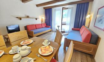 A modern living environment with light wood and colorful sofas. The table is festively set with dishes and a teapot.