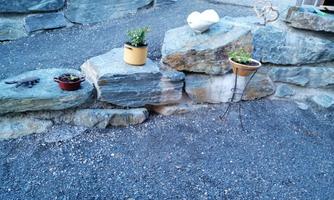 A small garden area with stones and various plant pots. The plants are arranged in colorful pots, surrounded by gravel.