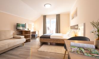 A modern room with a bed, a sofa, and a desk. Large windows provide plenty of natural light.