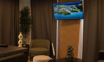 A modern living space with a cozy armchair and a round table. A television is hanging on the wall, displaying a landscape.