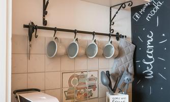 A modern kitchen with a coffee machine and hanging cups. Shelves display glasses and kitchen utensils in an inviting atmosphere.