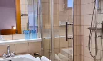 A modern bathroom with a glass shower cabin. Several glass bottles are on the sink and a towel is readily available.