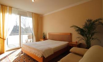 A bright bedroom with a large window and a cozy atmosphere. The room is decorated with a double bed, a sofa, and a plant.