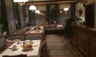 A cozy breakfast room with wooden furniture and colorful lamps. On the tables, there is a selection of fresh rolls and drinks.