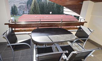 A beautiful balcony with a table and four chairs. In the background, green trees and a peaceful landscape can be seen.