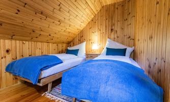 A cozy bedroom with two single beds and wooden paneling. The beds are decorated with blue blankets and white pillows.