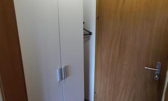 A small hallway with a white cabinet and a wooden door. The walls are light and the floor is made of wood.