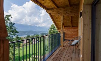 A sunny balcony with a wooden floor and a modern railing. In the background, a picturesque landscape with mountains and a lake stretches out.