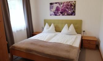 A cozy bedroom with a large bed and two pillows. A picture of purple flowers hangs on the wall.