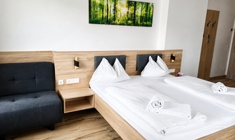 A modern bedroom with two beds and a cozy sitting area. A picture of a green forest hangs on the wall.