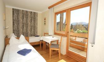 A bright room with two beds and a small table. Large windows offer a view of the surroundings.