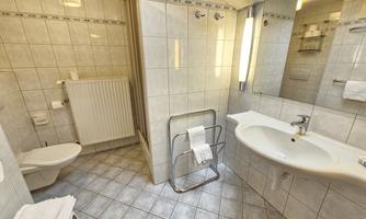 A modern bathroom with beige tiled walls. It features a shower, a sink, and a toilet.
