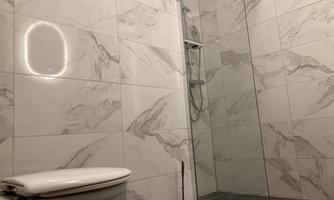 A modern bathroom with an elegant tile pattern. There is a shower with a glass partition and a toilet.