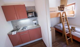 A cozy little kitchen with modern appliances and a lower bed. Above is a loft bed with two plush bears.