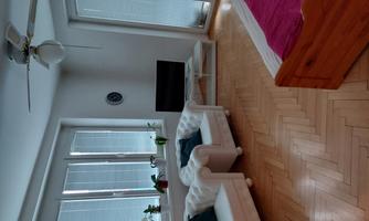 A bright living room with two white armchairs and a television. Large windows ensure plenty of daylight.