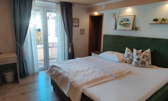 A modern bedroom with a large bed and soft colors. The room has access to a balcony and is well lit.