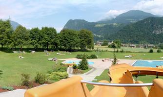 A spacious garden landscape with a swimming pool and many deck chairs. In the background, there are mountains and a clear sky.