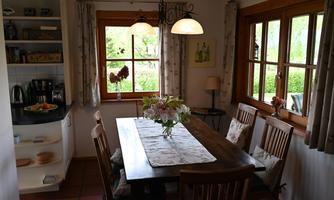 A cozy dining area with a large wooden table and chairs. The windows let in plenty of natural light and offer a view of the garden.