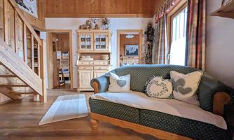 A cozy living room with a blue sofa and decorative cushions. In the background, there are wooden shelves and windows with curtains.