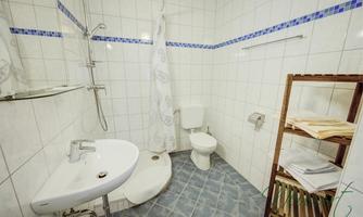 A modern bathroom with a shower, sink, and toilet. The walls are brightly tiled, and there is a shelf for towels.