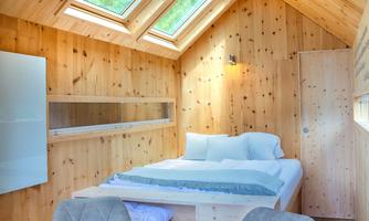 A cozy interior with wood paneling and large windows. There is a bed and a small table with chairs.