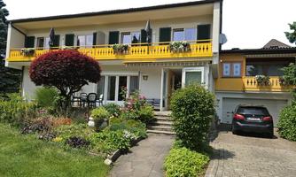 A beautiful house with a colorful garden and a yellow terrace. A car is parked on the path in front of the house.