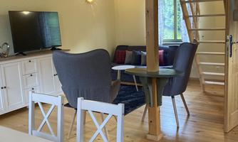 A cozy living space with wooden structure and stairs. There is a sofa, a television, and a dining table.
