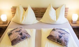 A cozy bedroom with a double bed and large pillows. The decorative pillows feature images of a deer.