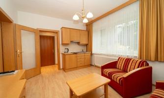 A cozy living space with a kitchenette and a dining table. The decor consists of wood and comfortable furniture in warm colors.