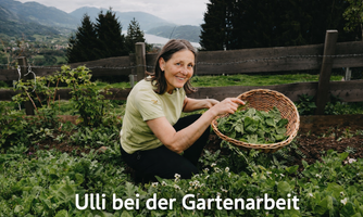 A woman is gathering fresh vegetable leaves in a garden. In the background, mountains and trees can be seen.