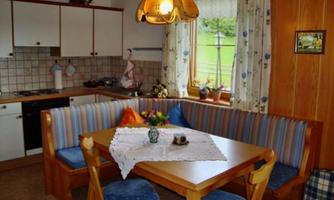 A cozy kitchen area with a wooden table and a bench adorned with colorful cushions. Additionally, there are plants and a lamp that create a warm atmosphere.