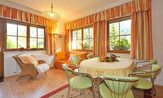 A cozy dining area with a round table and colorful chairs. Bright windows let in plenty of light, and colorful curtains create an inviting atmosphere.