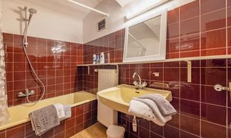 A modern bathroom with a red tiled floor. It includes a bathtub, a sink, and a mirror.