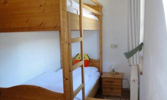 A simple bedroom with a bunk bed and a single bed. A wooden wardrobe and a small flower decoration complete the room.