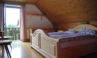 A cozy bedroom with a double bed and wooden furniture. From a balcony, there is a beautiful view of the surroundings.
