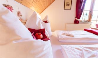 A cozy room with two beds and a warm wooden ceiling. A red apple is placed on one of the beds as decoration.
