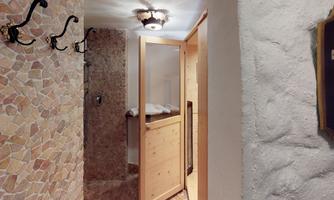 A cozy entrance area with a shower cabin made of wood and stone tiles. Several coat hooks are hanging on the wall.