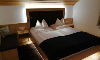 A cozy bedroom with a double bed and wooden paneling. On the left side, there is a small bench.