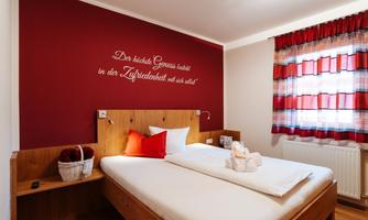 A cozy bedroom with a double bed and red accents. An inspiring quote is on the wall.