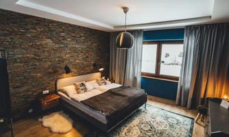 A modern bedroom with a stone wall and a large window. The stylish decor includes a comfortable bed and soft lighting.