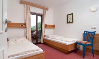 A simple room with two single beds and a blue chair. The room has a balcony and a friendly tone.