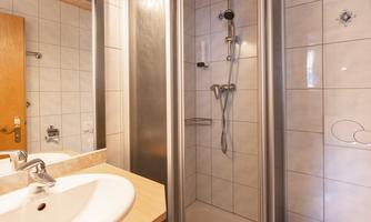 A modern bathroom with a shower cabin and a sink. The walls are tiled and there are wooden details.