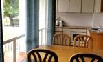 A cozy dining area with a wooden table and chairs. The windows offer a view of the greenery.
