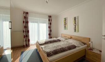 A modern bedroom with a double bed and two bedside tables. Large windows bring in plenty of daylight and the walls are decorated with beautiful pictures.
