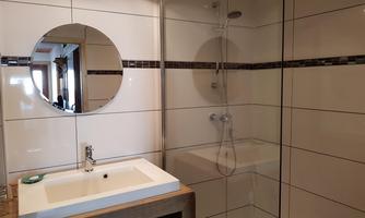 A modern bathroom with a shower and sink. The walls are tiled and there is a round mirror.