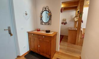 An inviting hallway with a wooden closet and a mirror. The walls are bright, and there is a warm wooden ceiling.