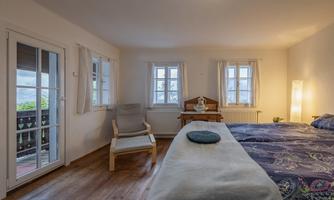 A bright bedroom with two windows and a large bed. A chair and a table complement the cozy furnishings.