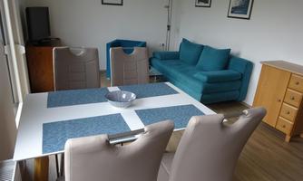 A modern living space with a dining table and ergonomic chairs. In the background, there is a green couch and there are some pictures on the wall.