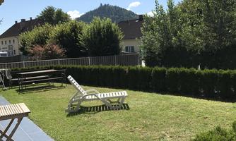 A quiet garden with a green lawn and a terrace. In the background, trees and a small hill are visible.