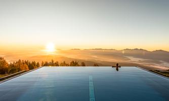 A modern pool with a view of the mountains at sunrise. The golden rays of sun reflect in the water.